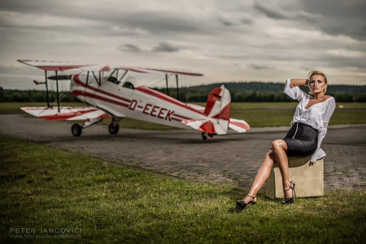 Woman seated on luggage beside a vintage biplane