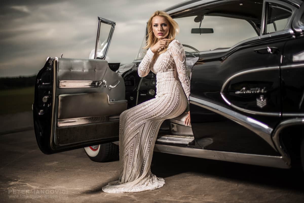 Woman in an evening dress beside a black vintage car